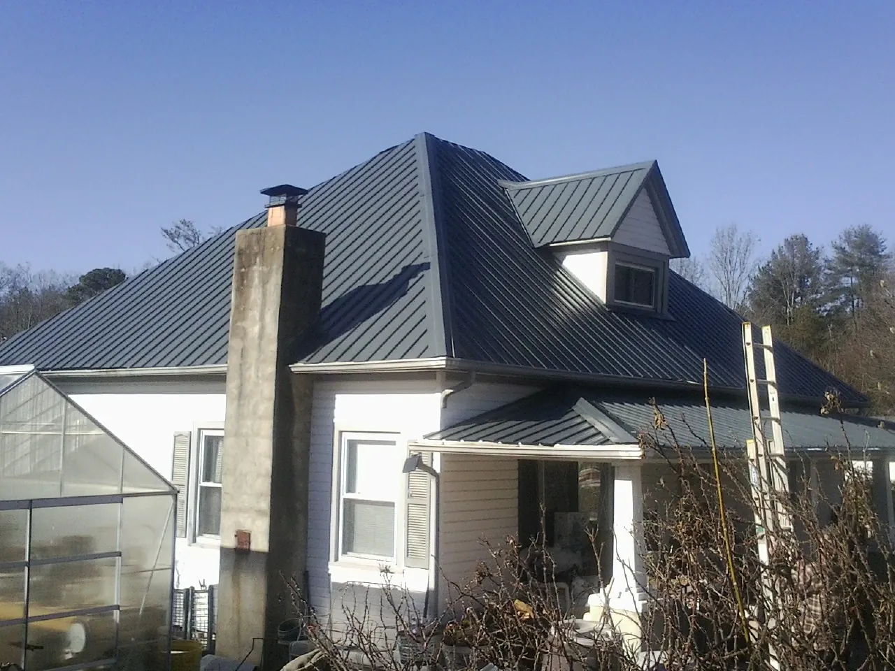 Dark blue standing seam metal roof on a white farmhouse with dormer — Slate & Tile Roof Repair by Roofing Brothers in Lowman