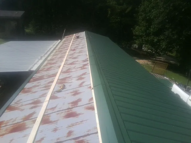 Old rusted panels beside newly installed green metal roofing — Wind Damage Roof Repair by Roofing Brothers in Lowman